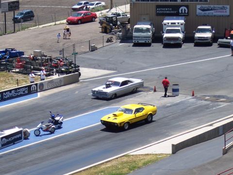 1972 Ford Ranchero - A yellow muscle car races down the drag strip, with a white classic car in the adjacent lane.