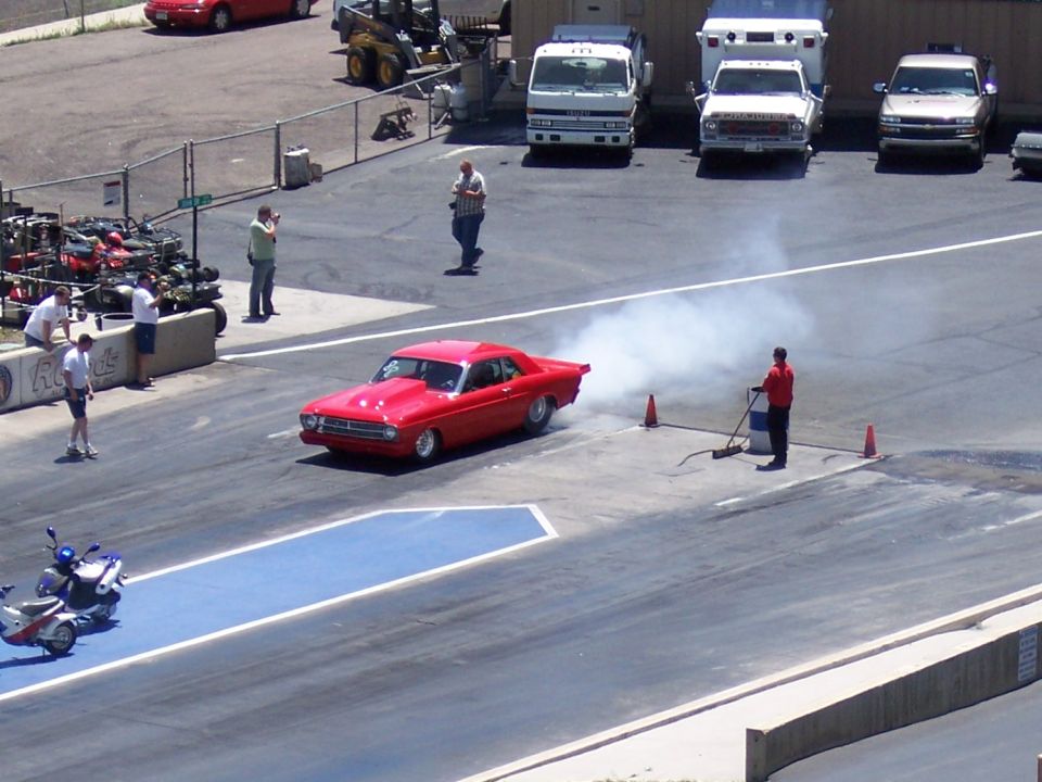 Red coupe with hood scoop doing a burnout on a drag strip