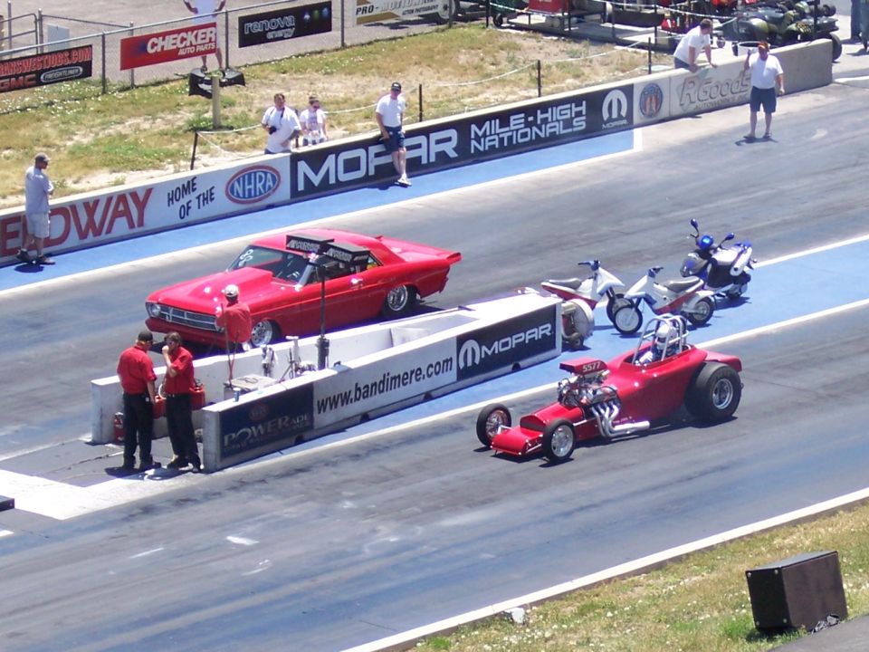 Drag strip with a red classic car, a dragster, and two scooters lined up