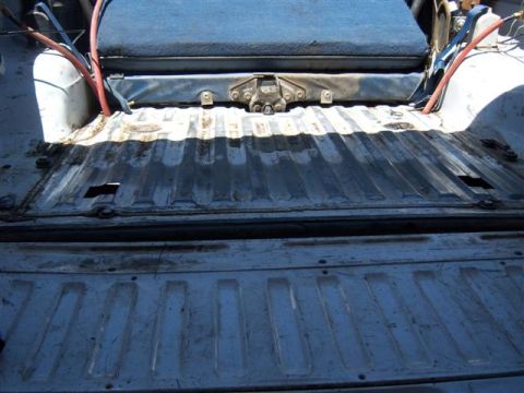 1995 Ford Bronco - The cargo area of a vehicle shows a ribbed metal floor and a blue upholstered seat.