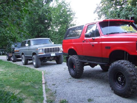 1979 Ford Bronco - Two lifted SUVs are parked on a gravel driveway, with trees in the background.