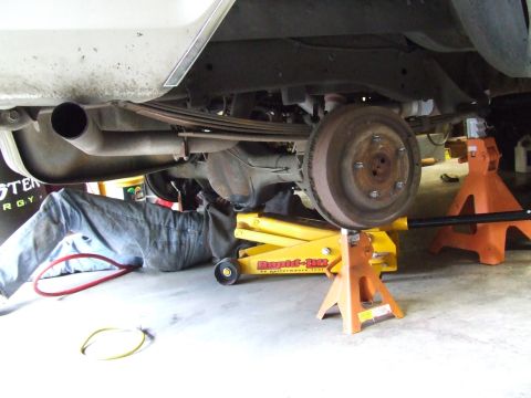 1979 Ford Bronco - Mechanic works on the rear axle and suspension of a vehicle supported by jack stands and a floor jack.