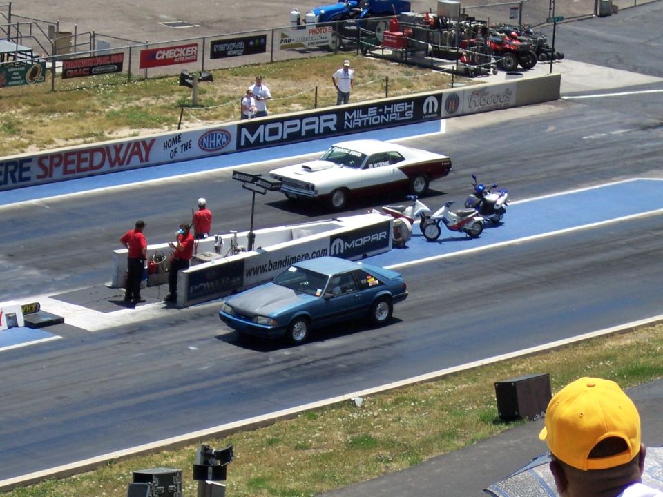 Blue hatchback drag car with gray hood, white car with maroon stripe, and two motorcycles on a drag strip