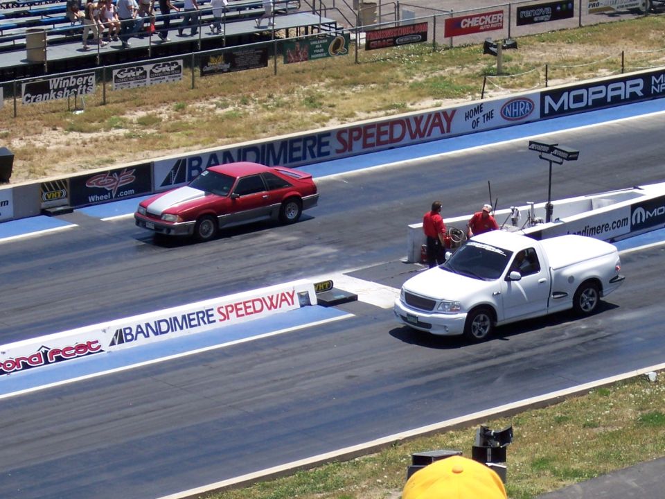 Red and silver car and white pickup truck race on drag strip at Bandimere Speedway