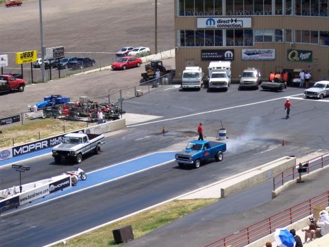 1972 Ford Ranchero - A blue pickup truck races down a drag strip, emitting smoke from its exhaust.