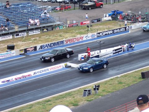 1972 Ford Ranchero - Two vehicles compete on the drag strip at Bandimere Speedway, with spectators in the stands.