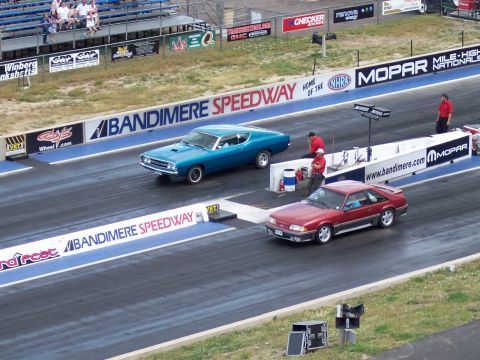 1972 Ford Ranchero - Two cars prepare for a drag race at Bandimere Speedway, with spectators in the stands.