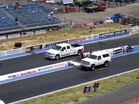 1972 Ford Ranchero - Two white Ford trucks are on the drag strip at Bandimere Speedway, with a motorcycle on a trailer behind the Bronco.