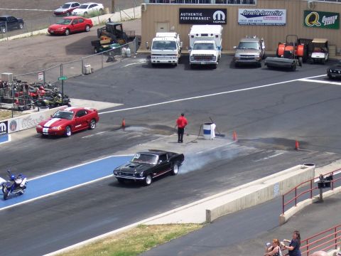 1972 Ford Ranchero - A black 1969 muscle car performs a burnout on the drag strip, with a red Mustang and a scooter nearby.