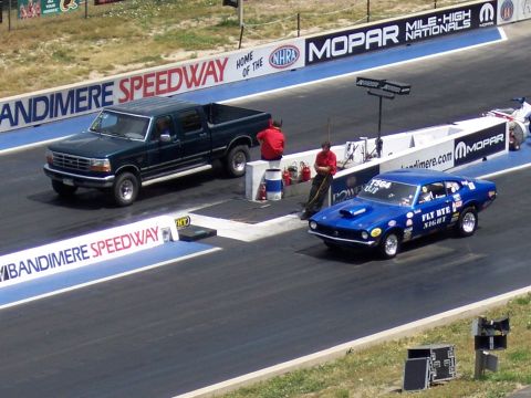 1972 Ford Ranchero - A blue muscle car races down the drag strip, with a dark green pickup truck in the adjacent lane.
