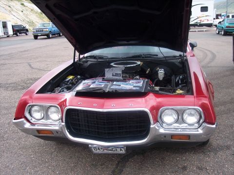 1972 Ford Ranchero - A red 1972 Ford Ranchero is displayed with its hood open, revealing the engine and a photo album on the engine bay.