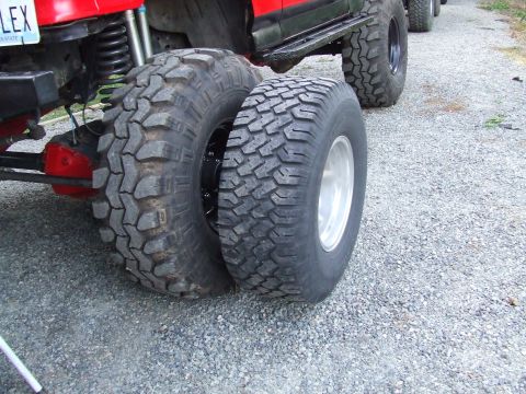 1979 Ford Bronco - A red SUV with oversized tires is parked on a gravel surface, with another vehicle visible in the background.