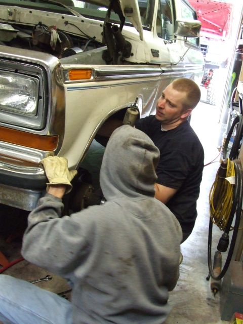 1979 Ford Bronco - Mechanics work on the front end of a lifted 1979 Ford Bronco in a garage.