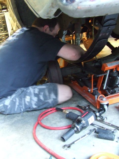 1979 Ford Bronco - Mechanic performing maintenance on vehicle suspension system, tools laid out on the ground.
