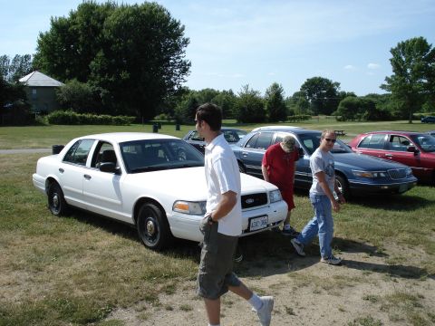 2000 Ford Crown Victoria - Several cars are parked on a grassy area under a clear sky.