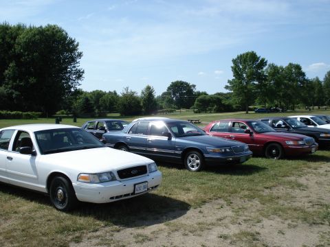 2000 Ford Crown Victoria - A white 2000 Ford Crown Victoria is parked in a line with other vehicles on a sunny day.