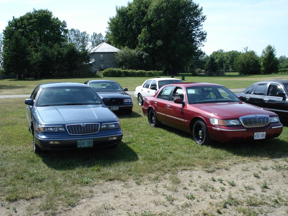Red Mercury Grand Marquis parked in grass with other cars behind it