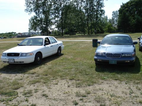 2000 Ford Crown Victoria - A white 2000 Ford Crown Victoria is parked next to a blue sedan on a grassy field.