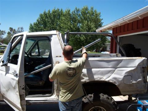 1995 Ford Bronco - A person is working on installing a rollcage into a white Ford Bronco that appears to be undergoing modifications.