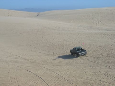 1990 Ford Bronco - A black Ford Bronco navigates sandy terrain under a clear blue sky.