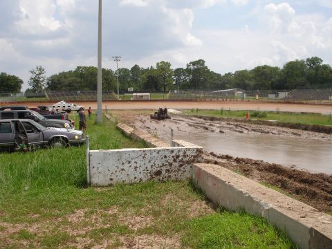 1989 Ford Bronco - Vehicles are parked on the grassy side of a mud bog track at a speedway.