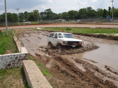 1989 Ford Bronco - White 1989 Ford Bronco navigates a muddy obstacle course at a speedway.