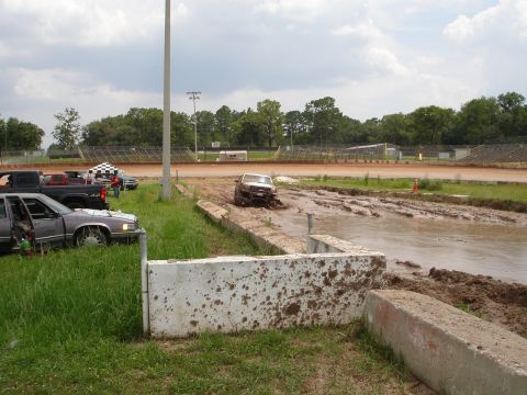 1989 Ford Bronco - A truck is stuck in a muddy track at a speedway, with several other vehicles visible in the background.
