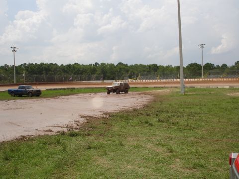 1989 Ford Bronco - A Ford Bronco navigates a muddy track at a speedway with a pickup truck nearby.