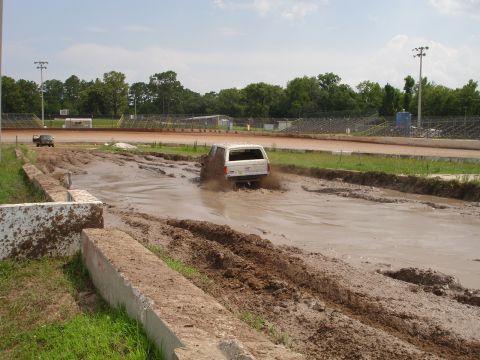 1989 Ford Bronco - A white SUV navigates a muddy track with spectators in the background.