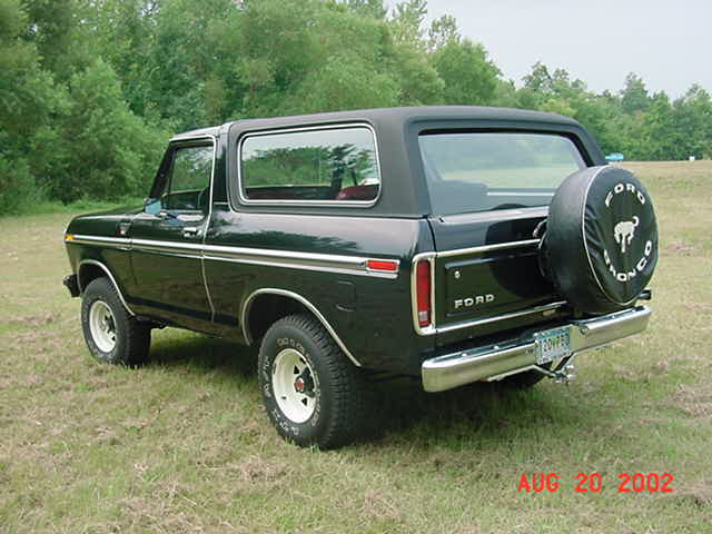 Black Ford Bronco with spare tire Bronco cover and white-spoke wheels, rear three-quarter view in a field