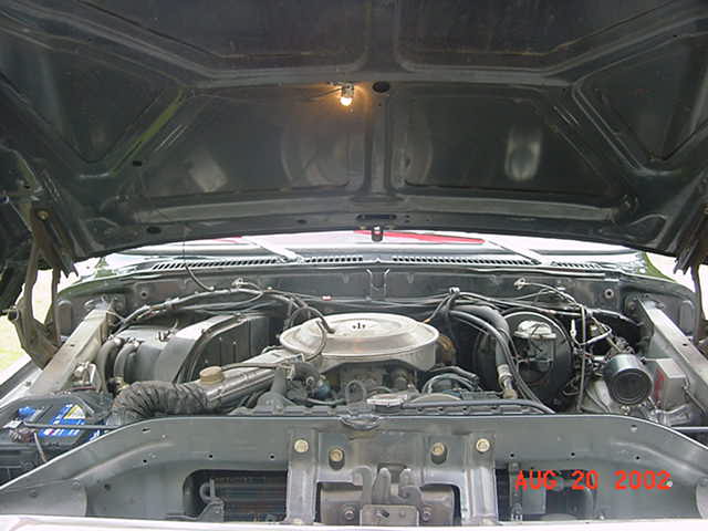 Engine bay of a vintage Ford truck with round air cleaner, hood raised, date stamp Aug 20 2002