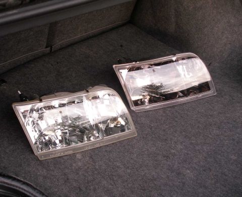 1998 Ford Crown Victoria - Two clear headlamp assemblies are shown, likely for a Ford Crown Victoria, resting in the trunk of a vehicle.