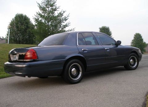 1998 Ford Crown Victoria - 1998 Ford Crown Victoria seen from the rear, parked on asphalt with trees in the background.