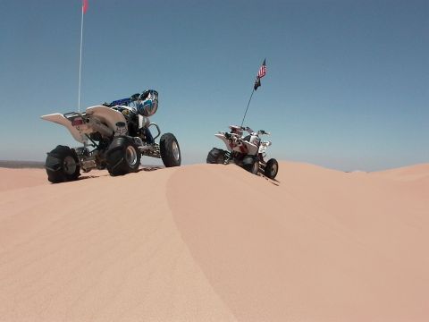 2003 Suzuki LTZ400 - Two quad bikes ride on sand dunes on a sunny day.