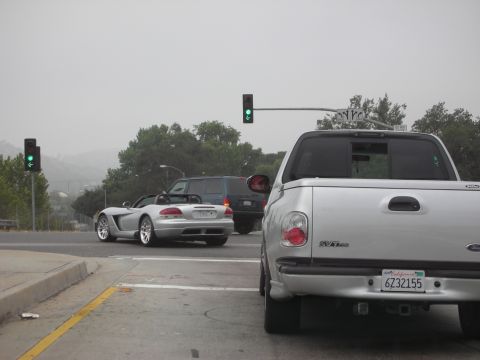 1998 Ford Crown Victoria - A silver convertible sports car is seen at an intersection, with a pickup truck in the foreground.