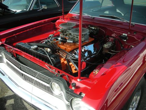 1998 Ford Crown Victoria - Engine bay of a red classic car, dual carburetors and a prominent grille. A second vehicle is partially visible.