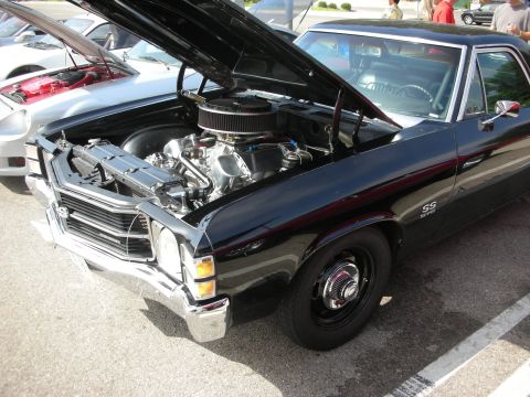 1998 Ford Crown Victoria - A black muscle car with its hood open, revealing a chrome V8 engine. Another vehicle is parked nearby.