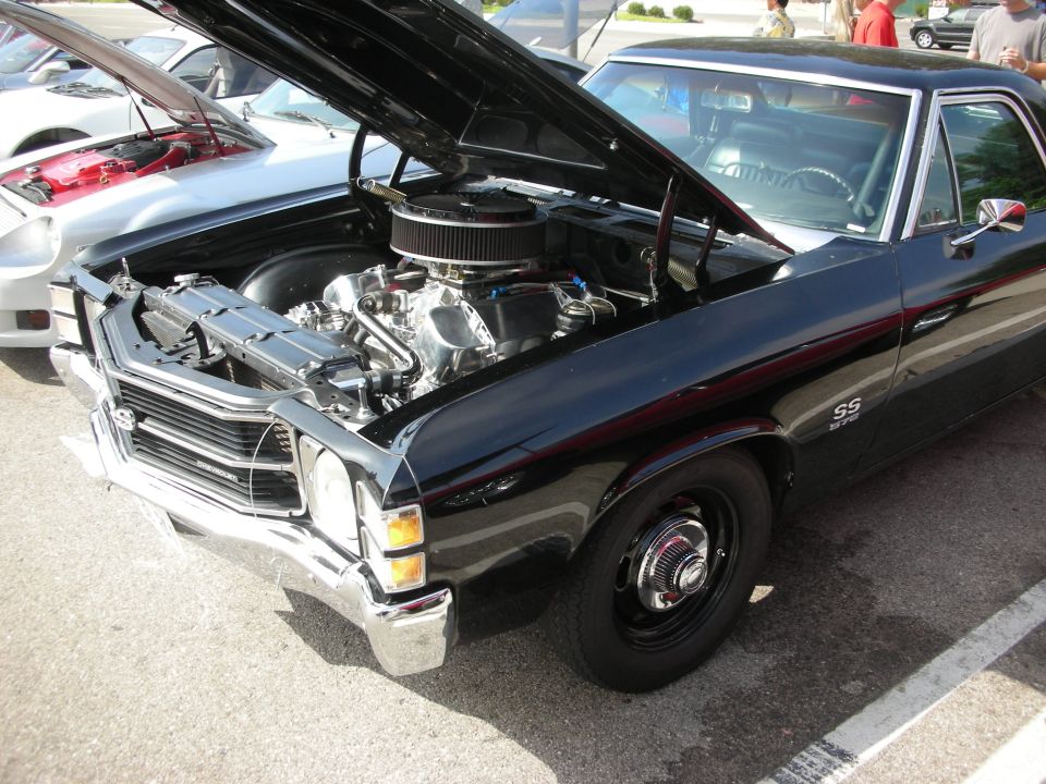 Black muscle car, hood open showing V8 engine. Another car with hood open is to the left