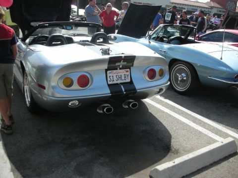 1998 Ford Crown Victoria - A silver convertible with black racing stripes and a "S1 SHLBY" license plate is parked next to a light blue classic car.