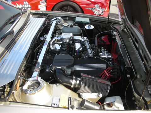 1998 Ford Crown Victoria - The engine bay of a car is shown, a chrome strut bar and an aftermarket air intake system. Another vehicle is visible in the background.
