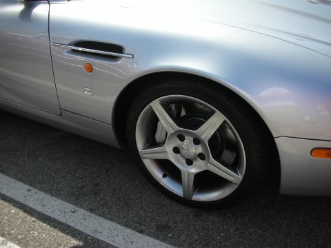 1998 Ford Crown Victoria - Close-up view of a silver sports car's front fender and wheel, showing a side vent and distinctive alloy wheel design.