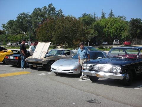 1998 Ford Crown Victoria - A black 1962 Chevrolet Impala is parked at a car meet, its distinctive chrome grille and red interior.