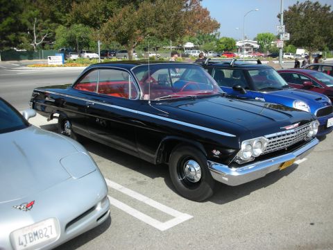 1998 Ford Crown Victoria - A classic black 1961 Chevrolet Impala is parked at a car meet with other vehicles.