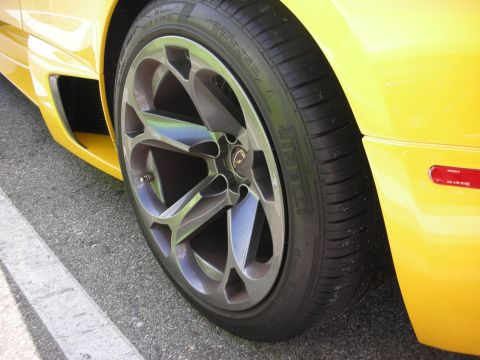1998 Ford Crown Victoria - Close-up of a yellow car's wheel, a Pirelli tire and a distinctive multi-spoke alloy rim.
