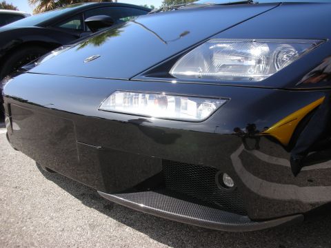 1998 Ford Crown Victoria - Close-up of a black sports car's front bumper and headlights, with another vehicle visible in the background.