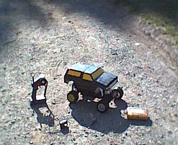 1989 Ford Bronco - A remote control car is shown on a gravel surface next to its controller.