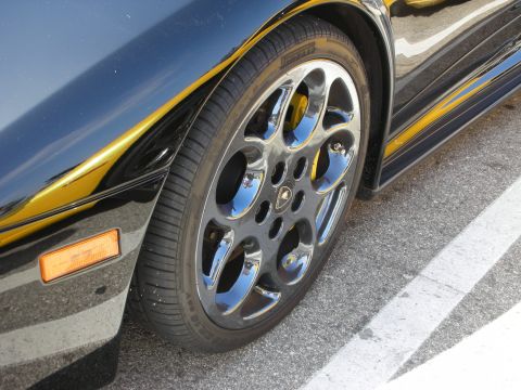 1998 Ford Crown Victoria - Close-up of a black car's front wheel and fender, showing a chrome rim and yellow brake caliper.