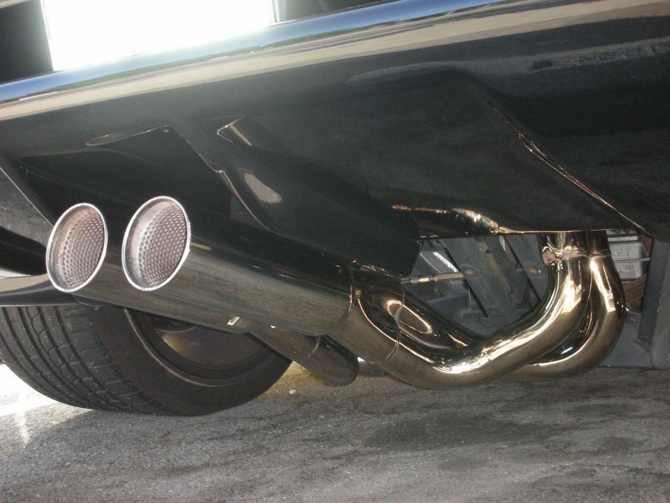 Underside view of a car's rear bumper with dual chrome exhaust tips and headers