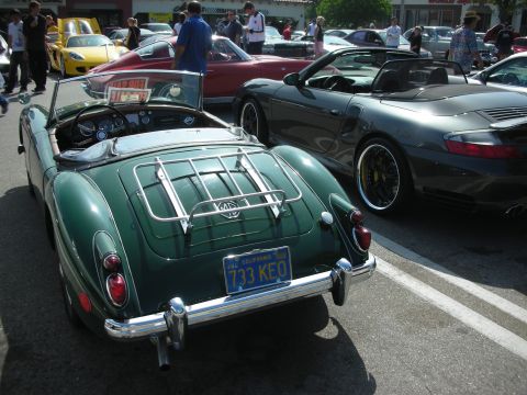 1998 Ford Crown Victoria - A classic green convertible is parked next to a modern sports car at an outdoor car meet.