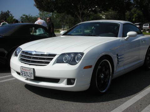 1998 Ford Crown Victoria - White Chrysler Crossfire coupe with custom wheels at a car meet. Another car is parked behind it.